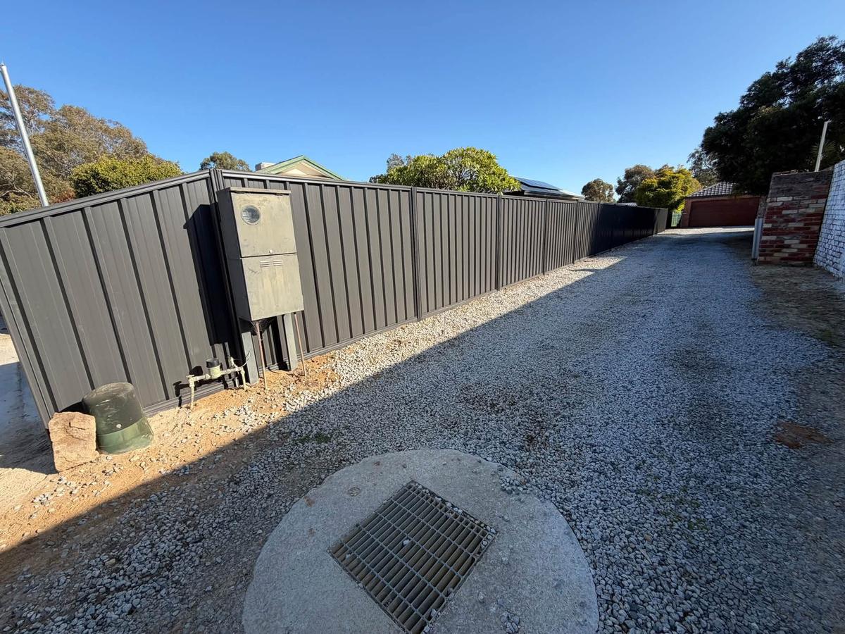 Dark Colorbond fence along a gravel driveway