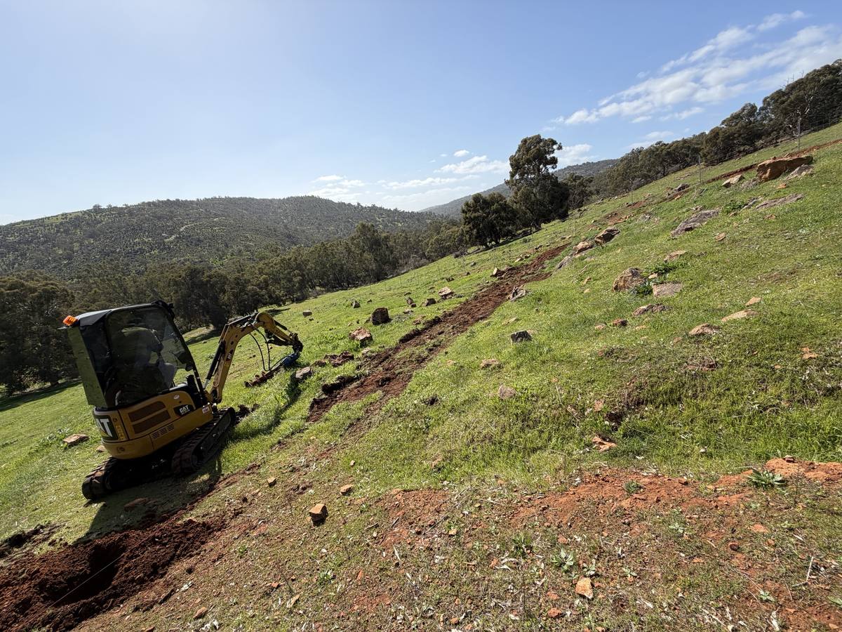 Mini excavator working a fence line on a Hills slope