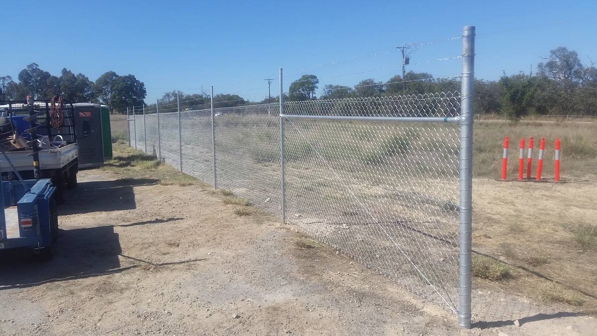 Galvanised chainmesh security fence with barbed wire on a commercial site