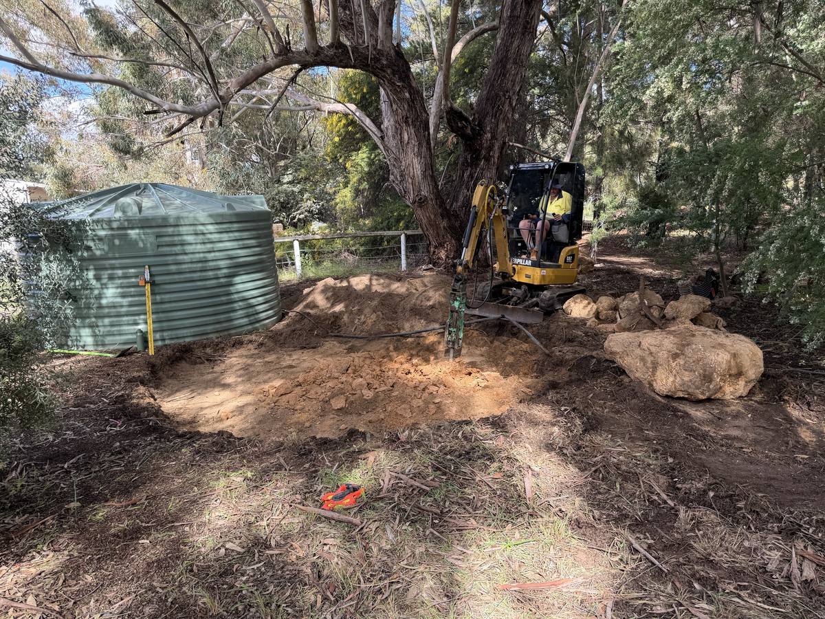 Mini excavator with rock breaker digging out a water tank pad